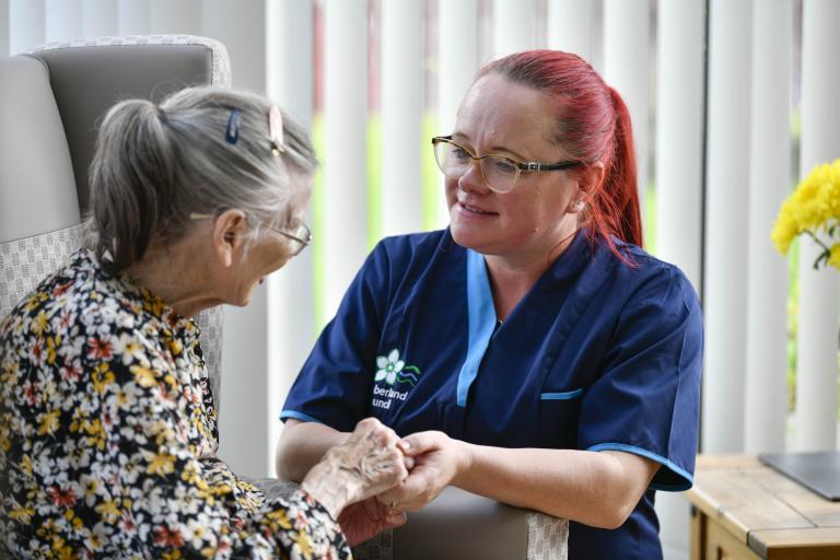 Carer with red hair hold hand of older lady