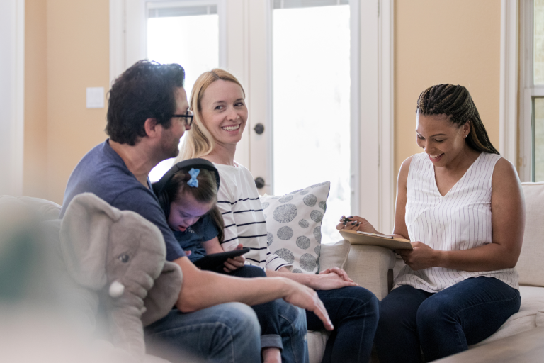 Woman with files talks to couple with daughter, daughter is watching a tablet