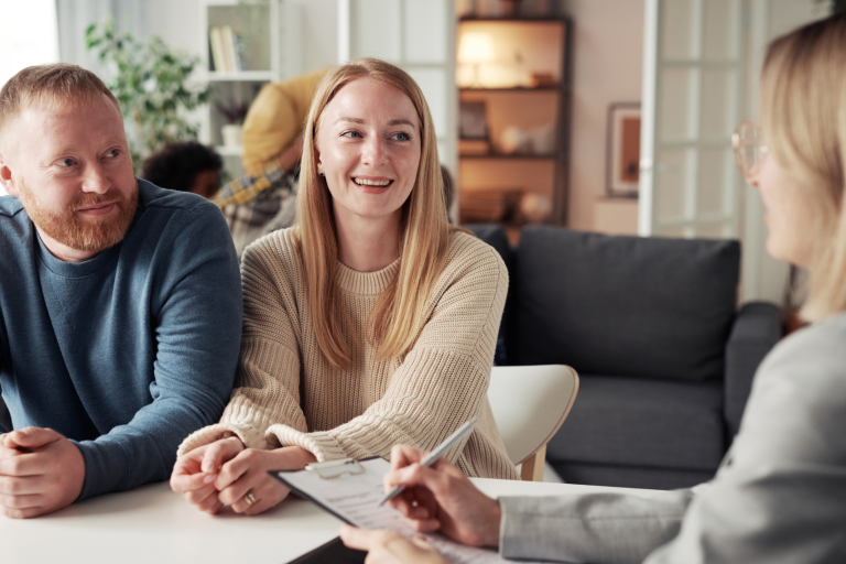 Couple talk to woman with paperwork, smiling across table