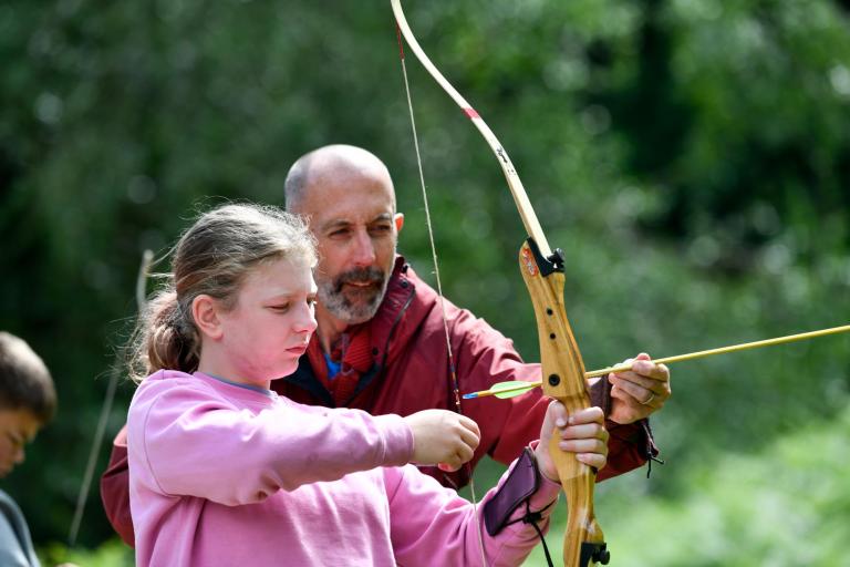 Man shows girl how to use bow and arrow